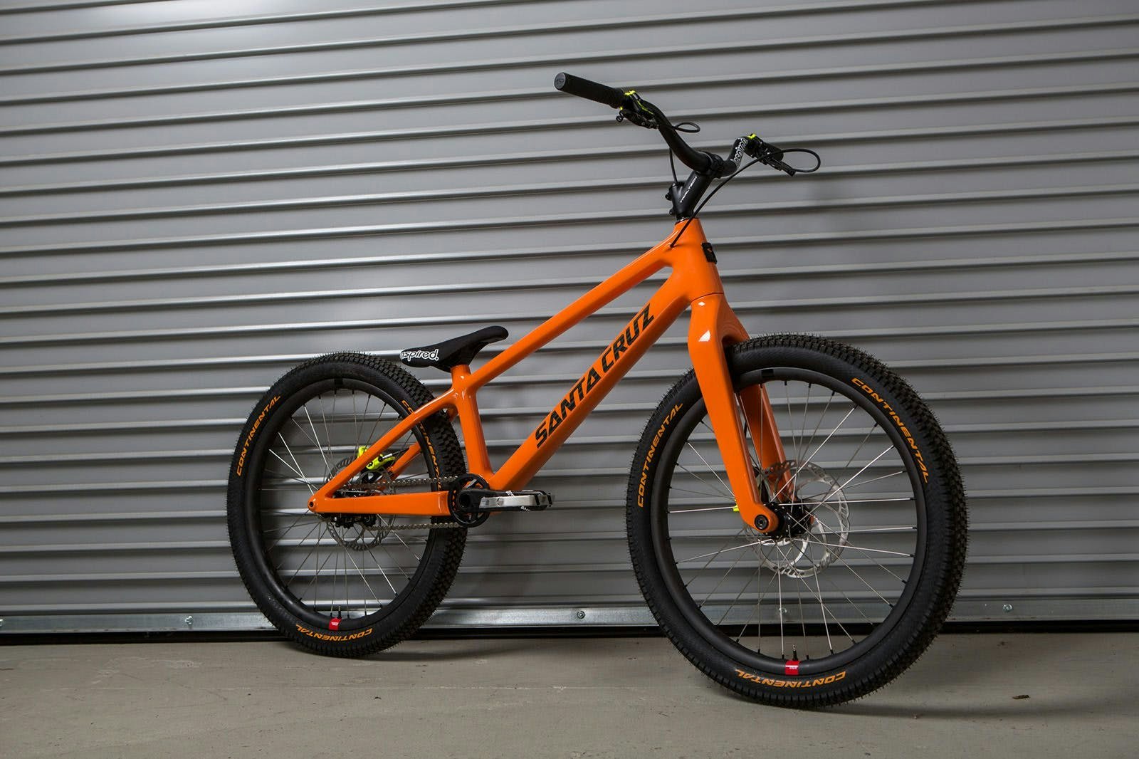 Danny Macaskill trails bike complete in orange with 24" Reserve carbon wheels in front of a Santa Cruz Bicycles factory roll up door