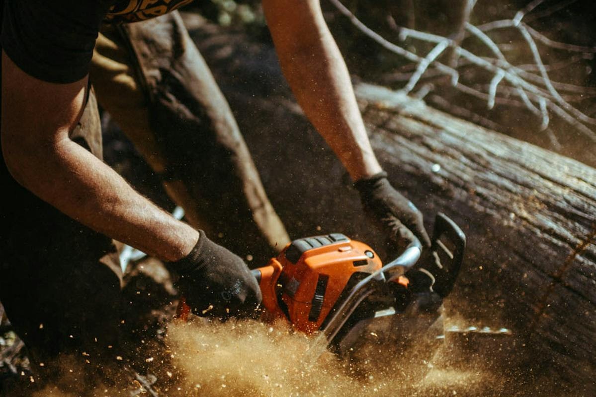 A trail builder cutting through a log with a chainsaw