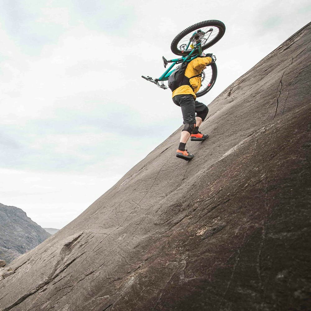 Danny MacAskill hiking up a rock slab with his 5010 on his back