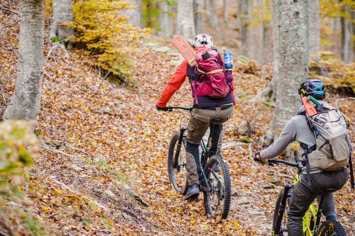 Two trailbuilders riding Heckler eMTB's with trail building tools in their backpacks