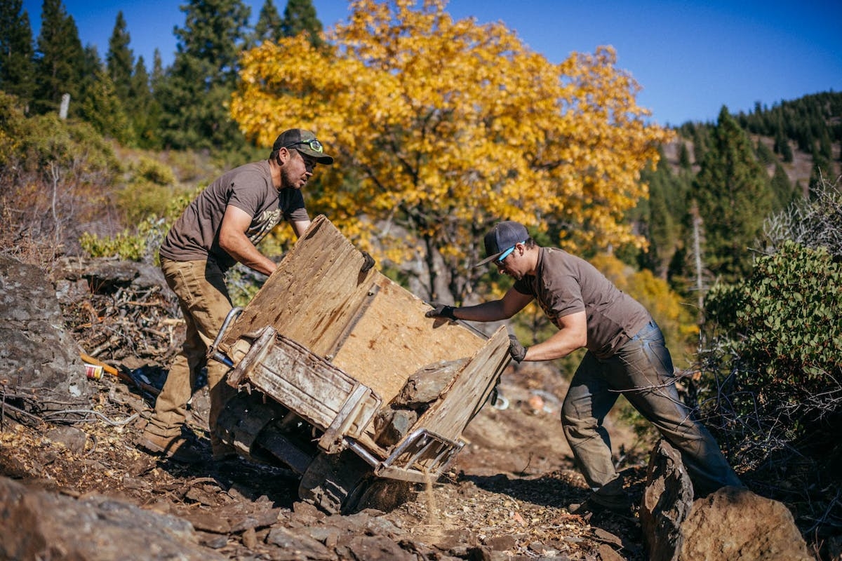 Two trail builders moving an old cart with wooden sides