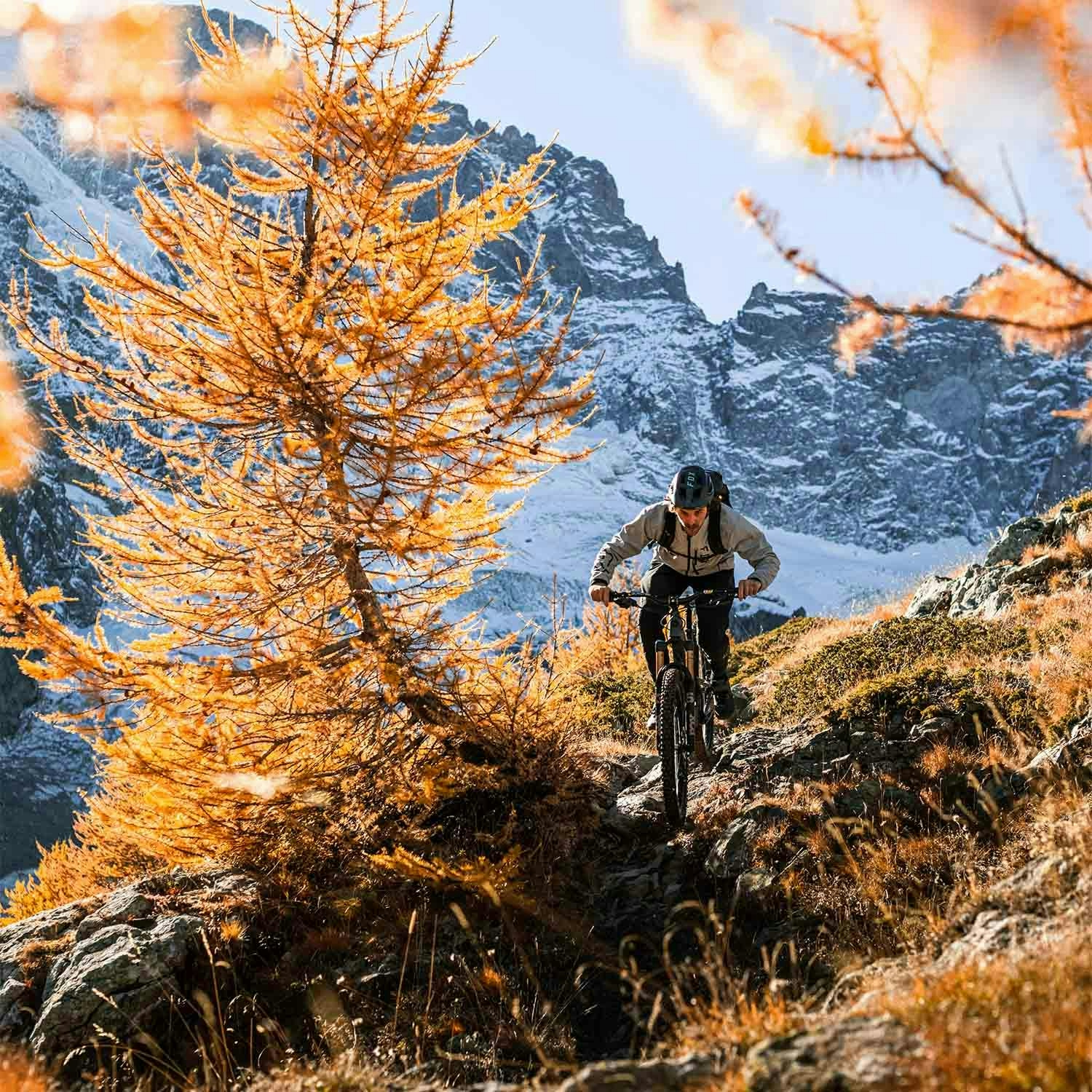 Loic D riding his mountain bike along a rocky trail with snowy mountains in the backdrop