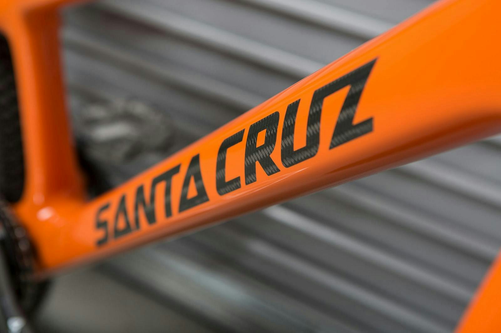 Close up of the downtube of the Danny Macaskill trails bike complete in orange with 20" Reserve carbon wheels in front of a Santa Cruz Bicycles factory roll up door