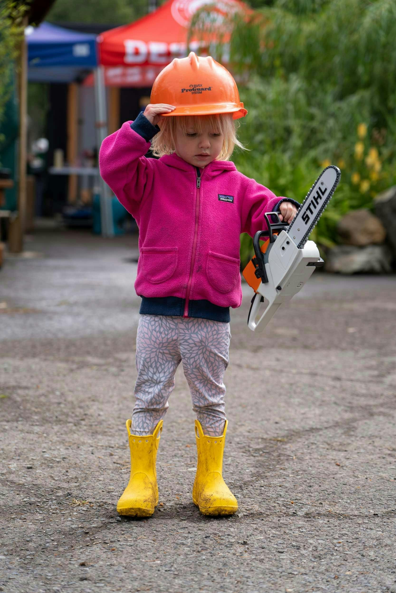 A young girl holding a child sized STIHL chainsaw