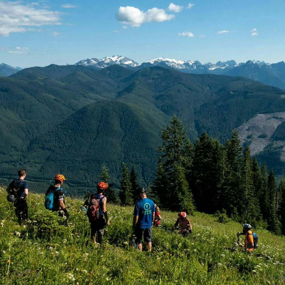 A group of mountain bikers standing together in a field with mountains in the background