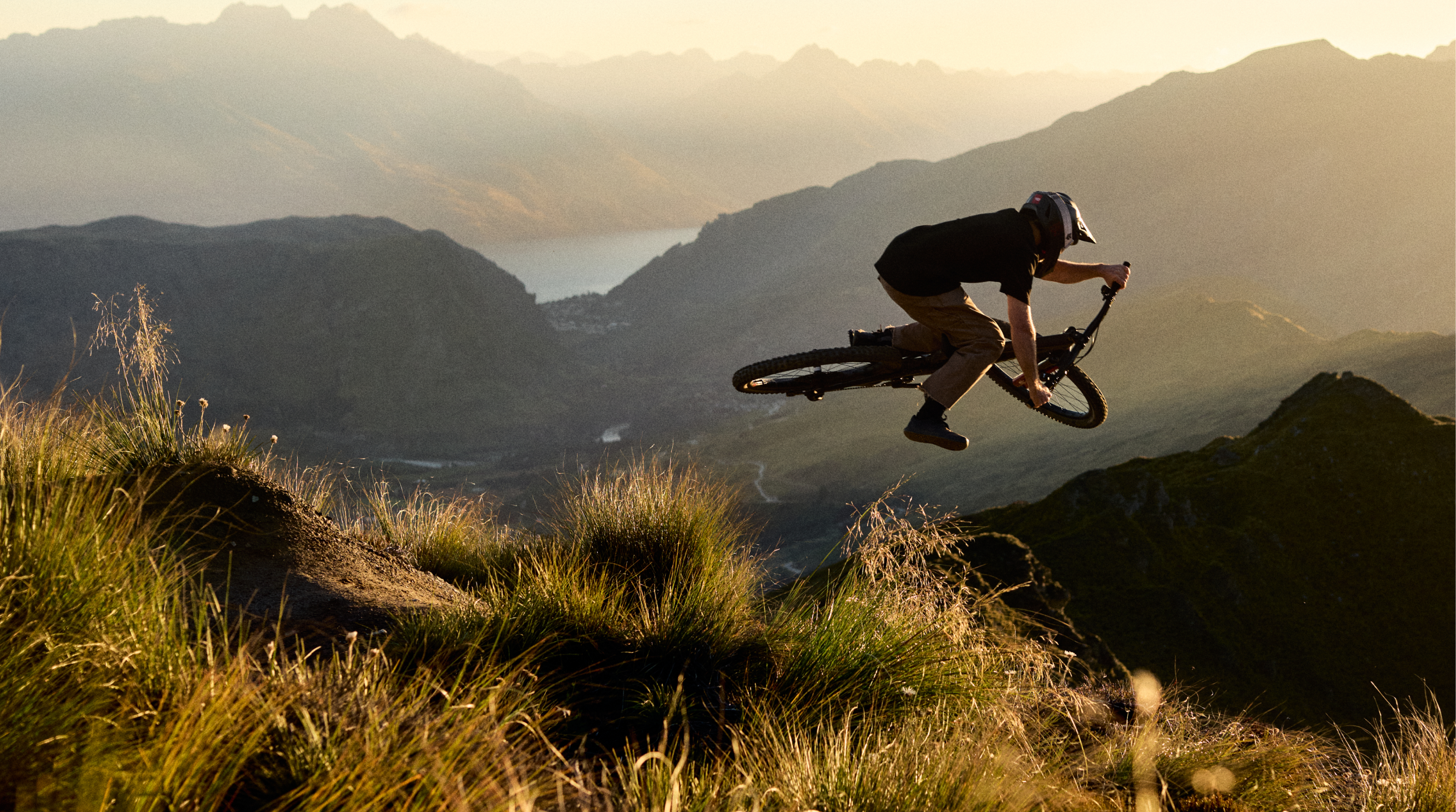 Person on a mountain bike performing a jump with mountains in the background