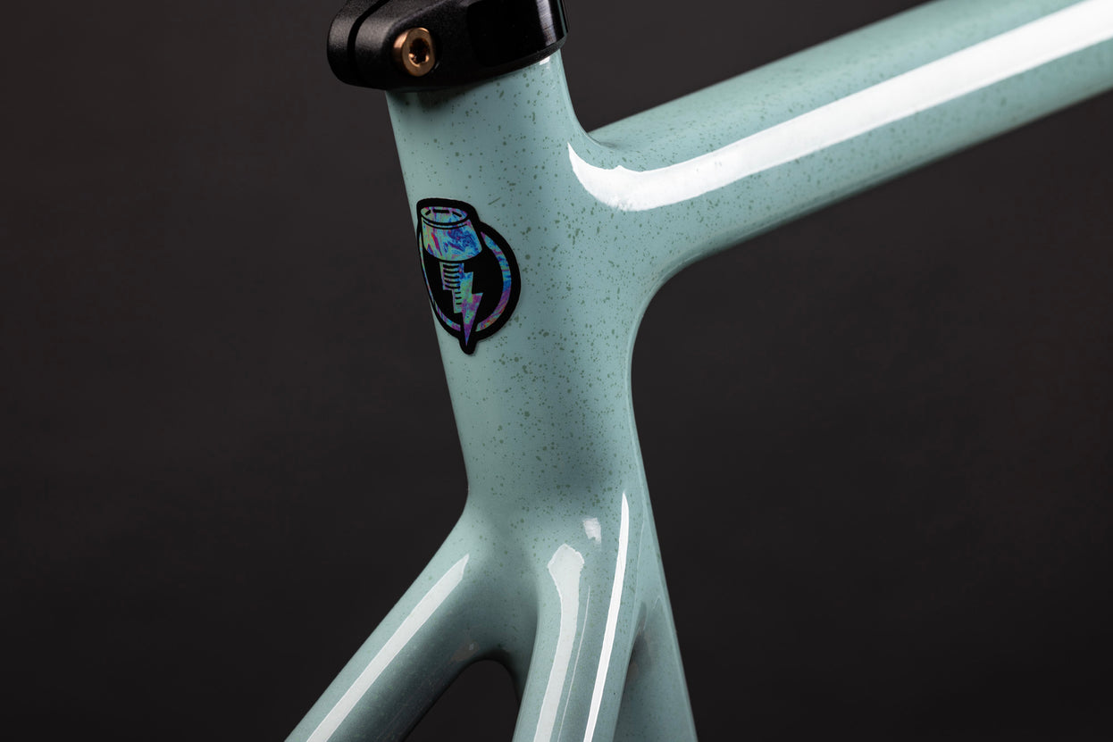 Close-up of a light blue bicycle frame with a logo on a dark background