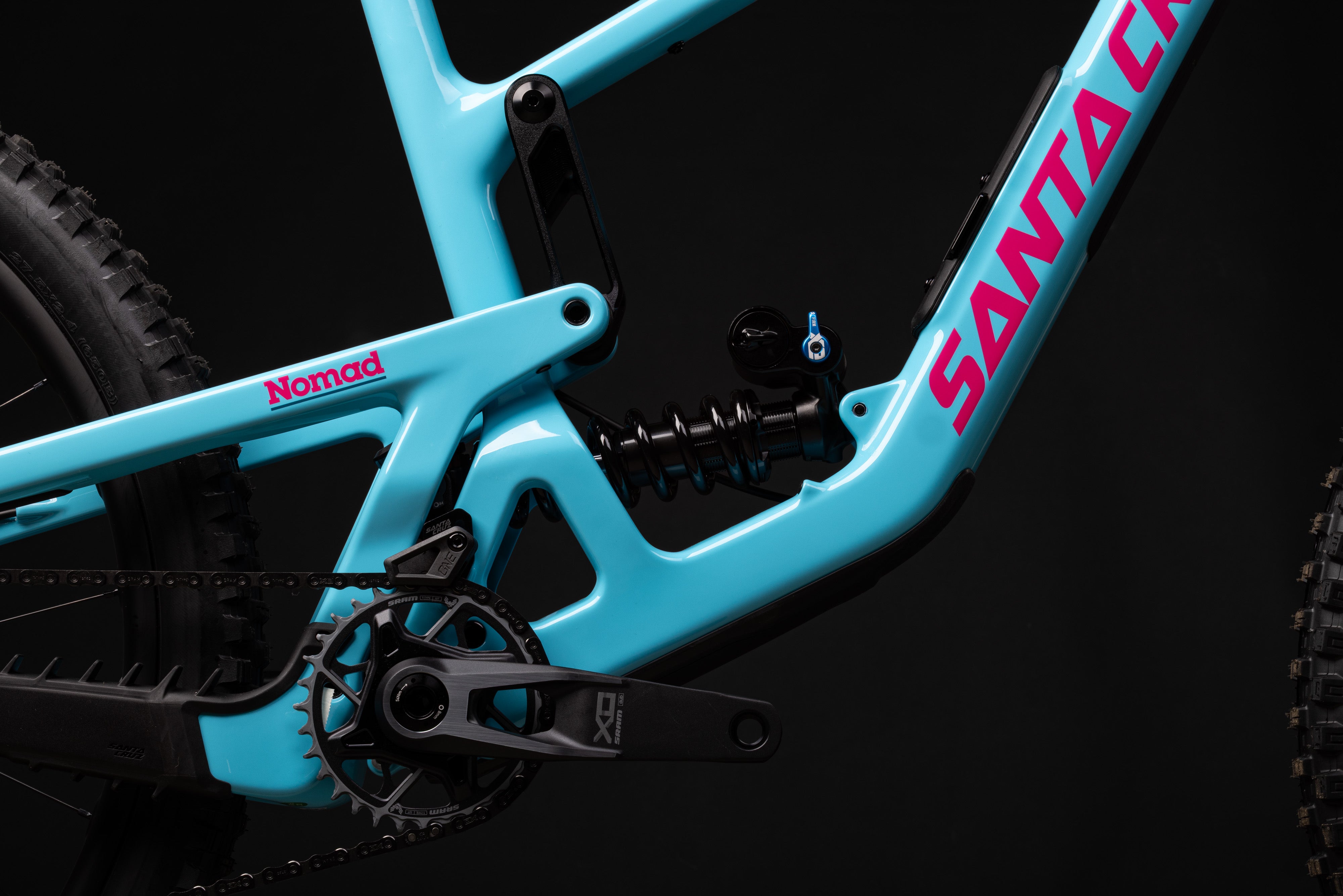 Close-up of a turquoise bicycle frame with 'Santa Cruz' and 'Nomad' branding on a black background.