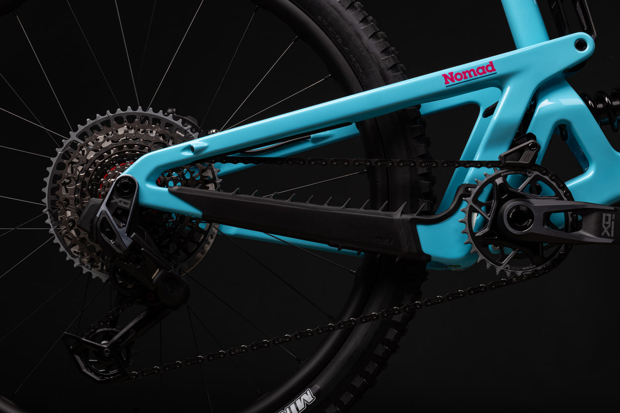 Close-up of a bicycle's chain and gear system with 'Nomad' branding on a black background.