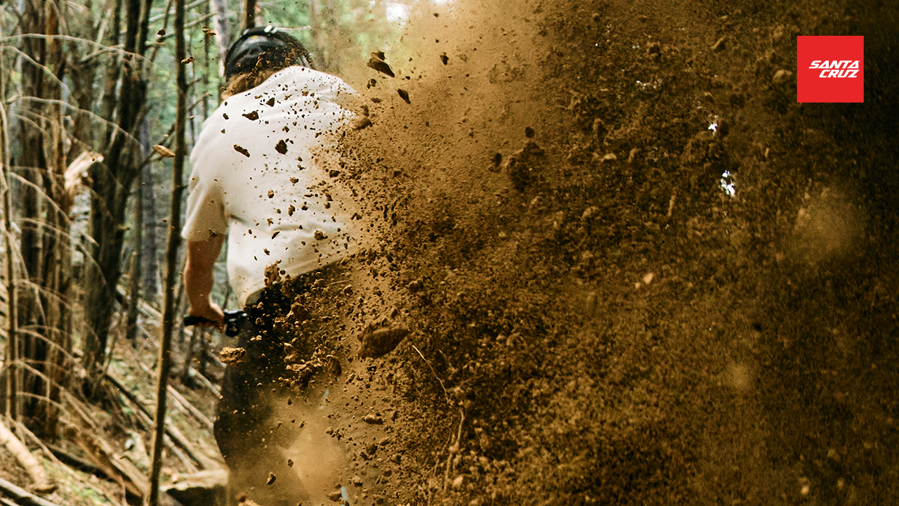 Person riding a bike through a muddy forest trail with 'Santa Cruz' branding.